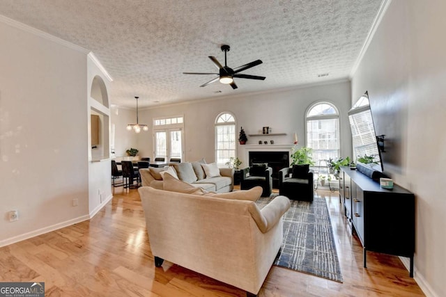 living room with a textured ceiling, ceiling fan with notable chandelier, ornamental molding, and light hardwood / wood-style floors