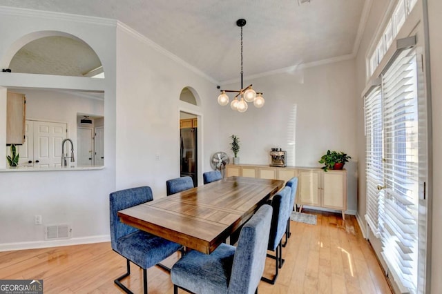 dining space with sink, light hardwood / wood-style flooring, crown molding, and an inviting chandelier