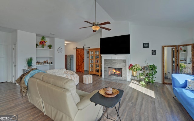 living room featuring wood-type flooring, built in shelves, a fireplace, ceiling fan, and a barn door