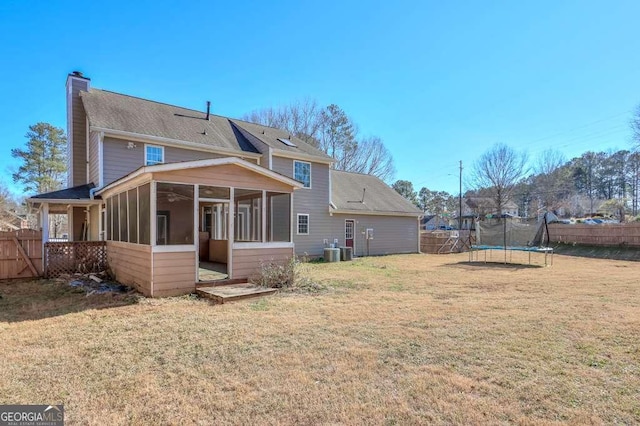 rear view of house with a lawn, central air condition unit, a trampoline, and a sunroom