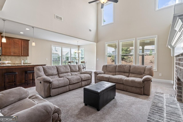 living room with a high ceiling, ceiling fan with notable chandelier, a fireplace, and light colored carpet