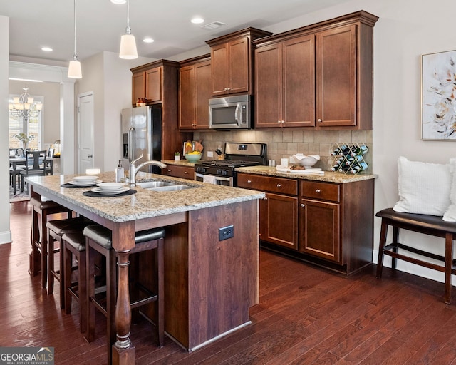 kitchen featuring a breakfast bar, pendant lighting, stainless steel appliances, a kitchen island with sink, and light stone countertops