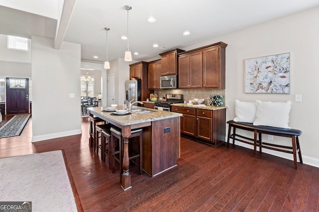 kitchen with dark wood-style flooring, pendant lighting, decorative backsplash, appliances with stainless steel finishes, and a kitchen island with sink