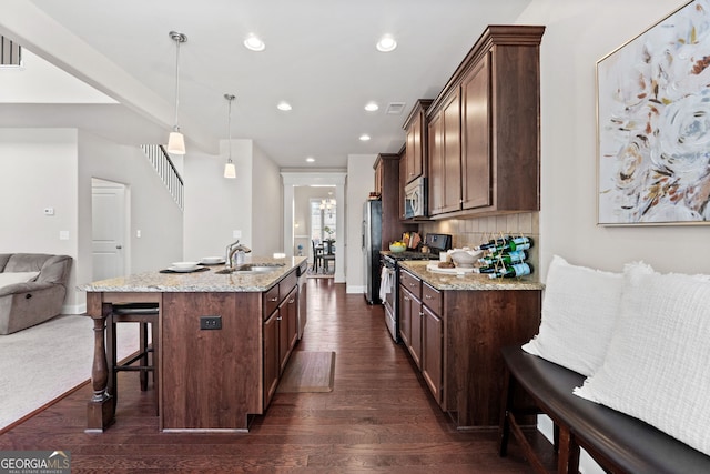 kitchen featuring a breakfast bar, pendant lighting, stainless steel appliances, a sink, and light stone countertops