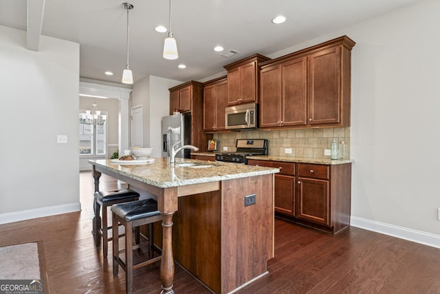 kitchen featuring appliances with stainless steel finishes, decorative light fixtures, backsplash, light stone counters, and a center island with sink