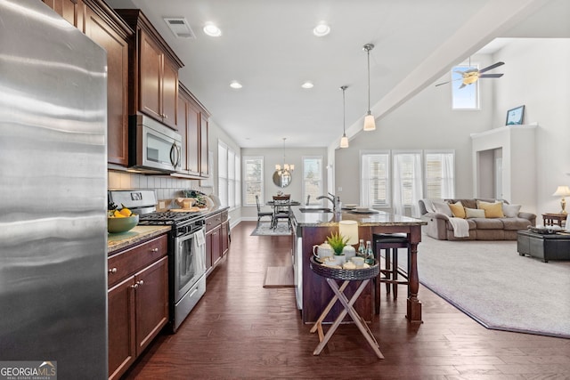 kitchen with an island with sink, decorative light fixtures, light stone countertops, stainless steel appliances, and a kitchen bar