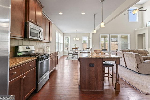 kitchen featuring a breakfast bar, hanging light fixtures, a kitchen island with sink, appliances with stainless steel finishes, and light stone counters