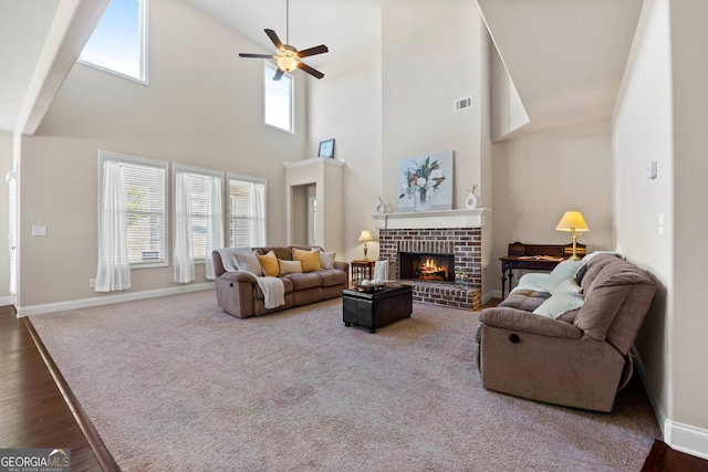 living area with a fireplace, visible vents, ceiling fan, wood finished floors, and baseboards