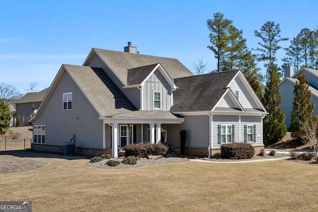 view of front of home with a chimney, fence, a front yard, board and batten siding, and brick siding