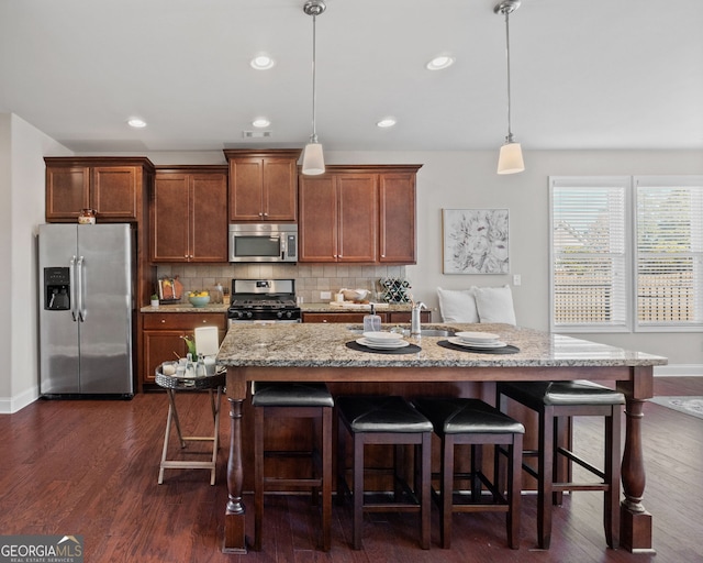 kitchen featuring stainless steel appliances, dark wood finished floors, a center island with sink, and decorative light fixtures