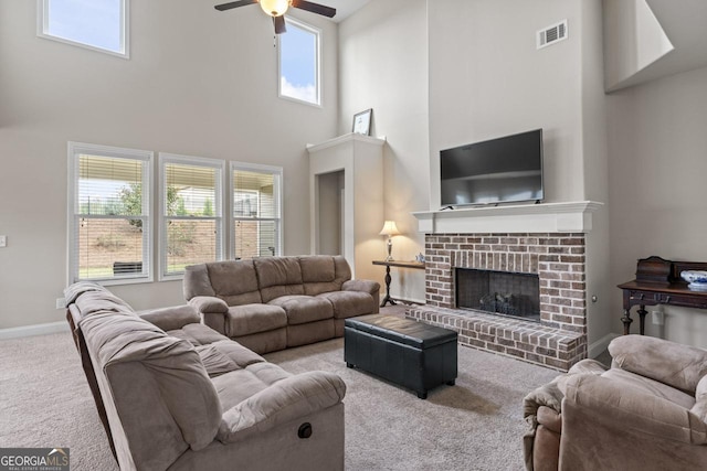 living room with ceiling fan, a high ceiling, carpet floors, and a brick fireplace