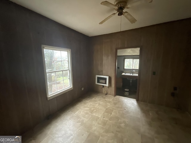 unfurnished room featuring ceiling fan, heating unit, and wood walls