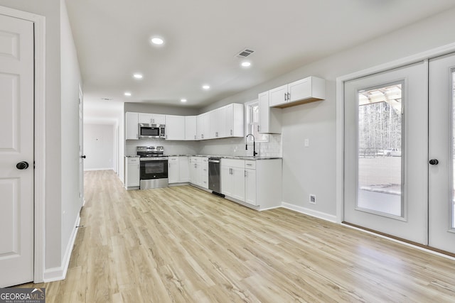 kitchen featuring tasteful backsplash, sink, light wood-type flooring, appliances with stainless steel finishes, and white cabinets