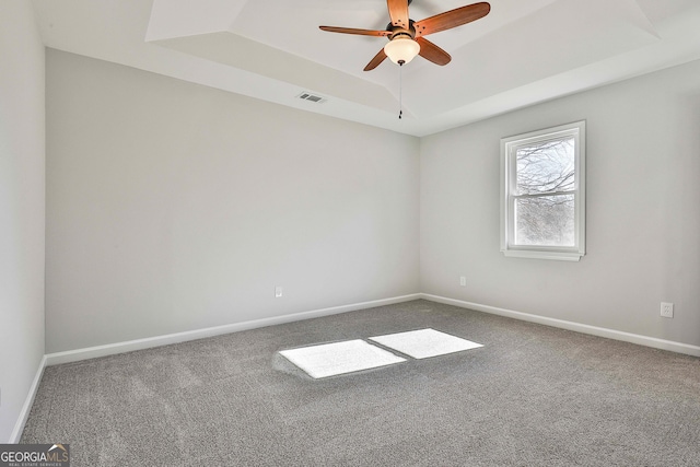 carpeted spare room with ceiling fan and a tray ceiling