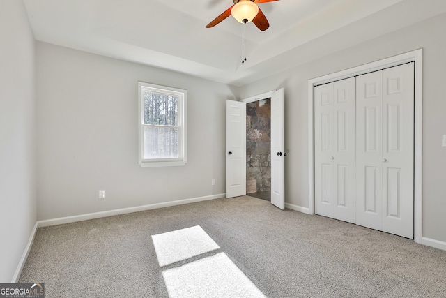 unfurnished bedroom featuring ceiling fan, a closet, light colored carpet, and a raised ceiling