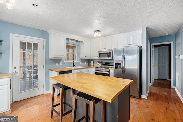 kitchen featuring sink, wooden counters, appliances with stainless steel finishes, white cabinetry, and a kitchen breakfast bar