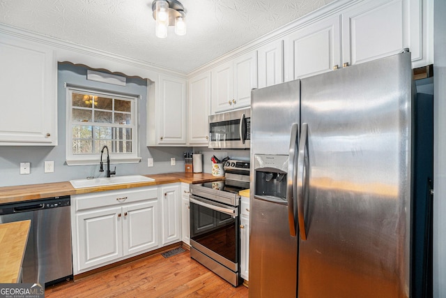 kitchen with stainless steel appliances, white cabinetry, butcher block counters, and sink