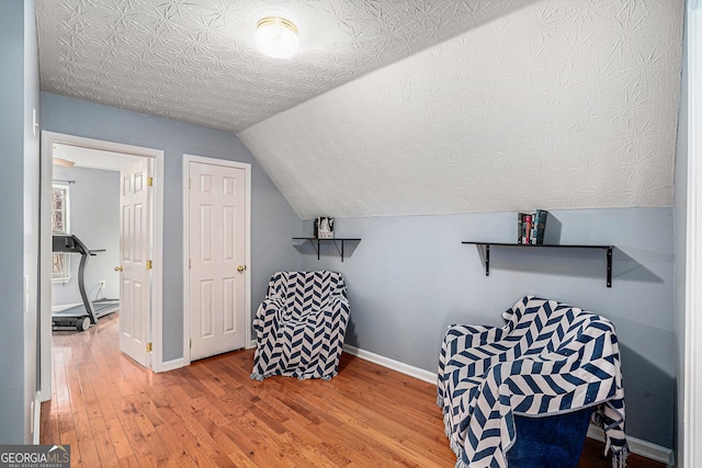 sitting room with hardwood / wood-style flooring, vaulted ceiling, and a textured ceiling