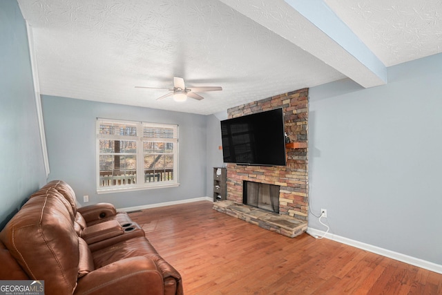 living room featuring hardwood / wood-style flooring, ceiling fan, a fireplace, and a textured ceiling