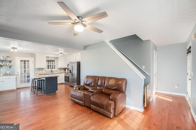 living room with ceiling fan, sink, a textured ceiling, and light wood-type flooring