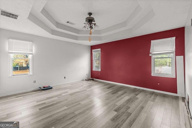 unfurnished room with ceiling fan, a tray ceiling, and light hardwood / wood-style flooring