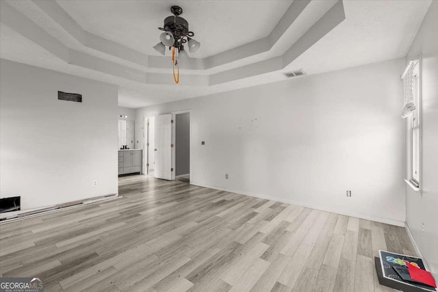 spare room with ceiling fan, light hardwood / wood-style flooring, and a raised ceiling