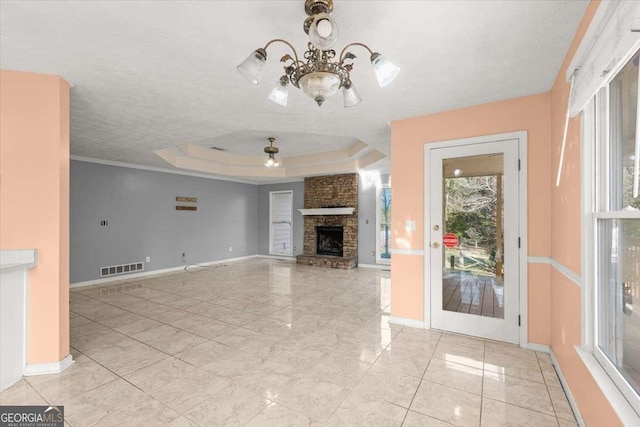 unfurnished living room with ceiling fan with notable chandelier, a textured ceiling, a tray ceiling, and a stone fireplace