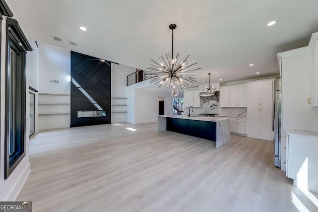 kitchen featuring pendant lighting, white cabinetry, light wood-type flooring, a kitchen island with sink, and a chandelier