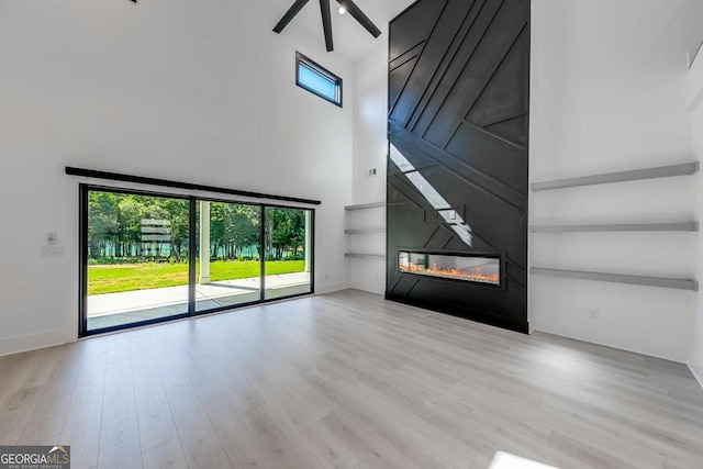 unfurnished living room with ceiling fan, a fireplace, a high ceiling, and light hardwood / wood-style flooring