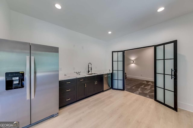 kitchen with appliances with stainless steel finishes, light wood-type flooring, french doors, light stone countertops, and sink