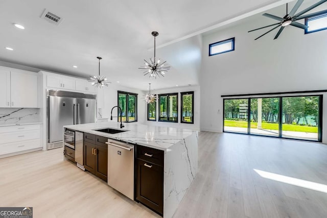 kitchen with appliances with stainless steel finishes, pendant lighting, ceiling fan with notable chandelier, white cabinets, and sink