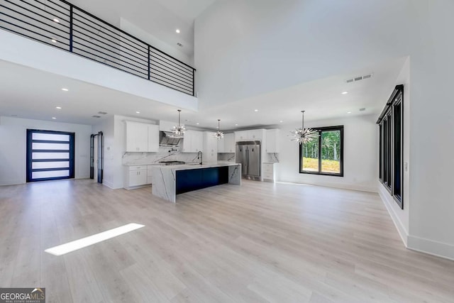 interior space with decorative light fixtures, a center island with sink, stainless steel refrigerator, white cabinetry, and a kitchen breakfast bar