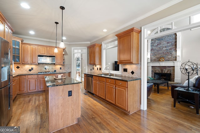 kitchen featuring a stone fireplace, hardwood / wood-style floors, decorative light fixtures, a center island, and stainless steel appliances