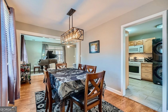 dining room featuring stacked washer and clothes dryer, an inviting chandelier, and light wood-type flooring