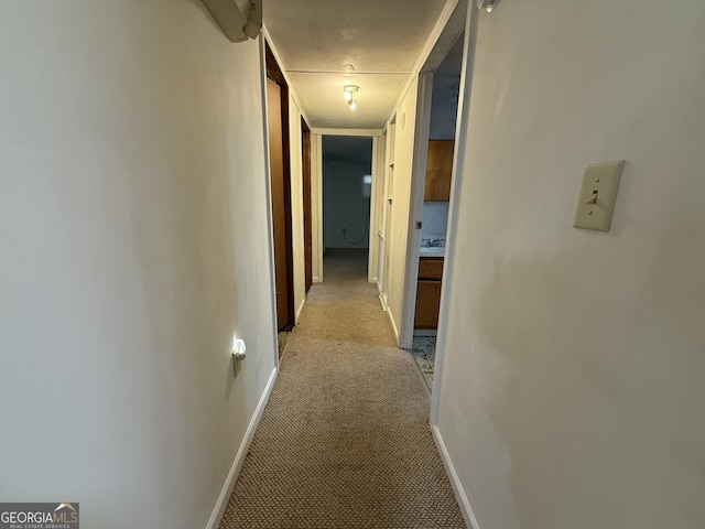 hallway featuring light colored carpet and baseboards