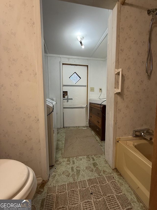 bathroom featuring a washtub, toilet, vanity, washer / dryer, and wallpapered walls