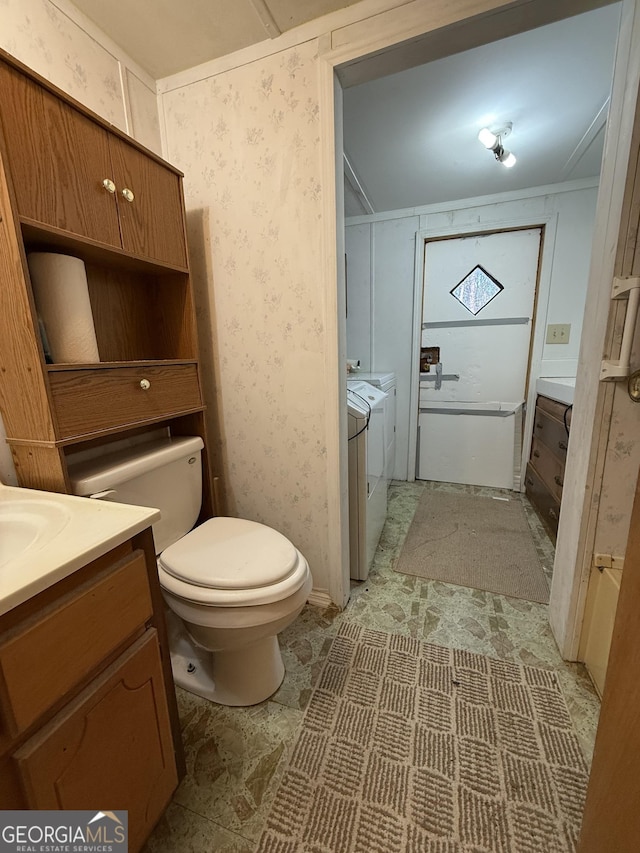 bathroom with toilet, wallpapered walls, washer and clothes dryer, and vanity