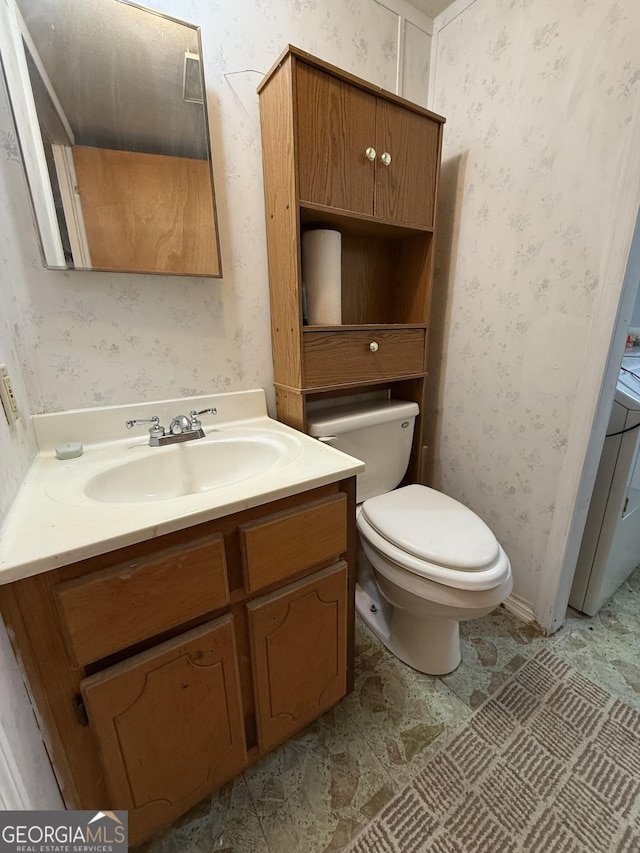 half bathroom with vanity, toilet, and wallpapered walls