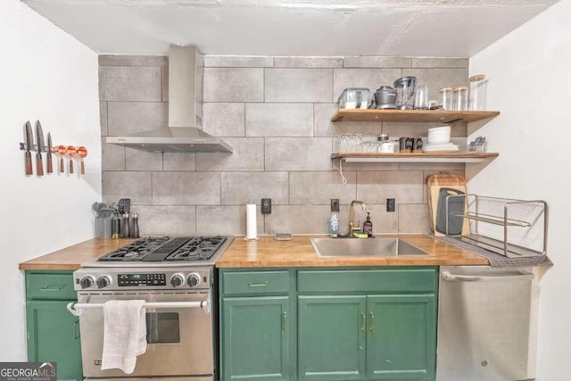 kitchen featuring appliances with stainless steel finishes, wall chimney exhaust hood, tasteful backsplash, sink, and green cabinetry