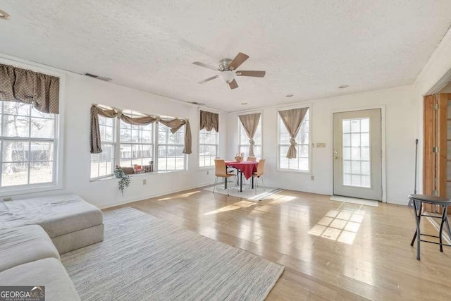 living room featuring ceiling fan, light hardwood / wood-style floors, and a textured ceiling