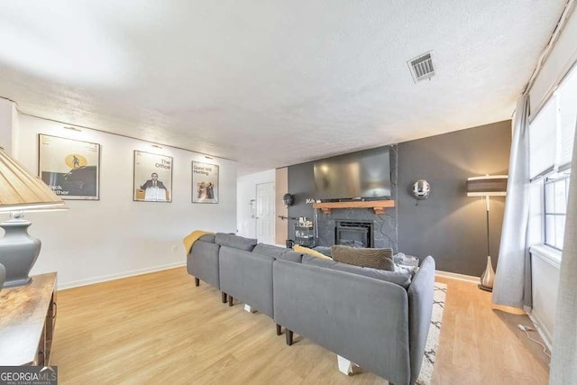 living room with a fireplace, a textured ceiling, and light wood-type flooring