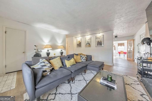 living room with a textured ceiling, ceiling fan, and light hardwood / wood-style floors