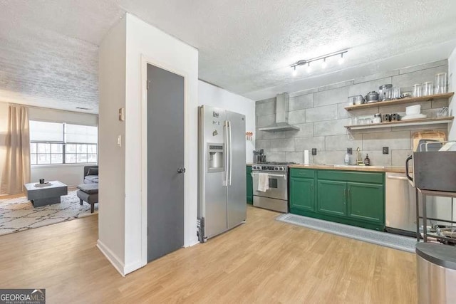 kitchen featuring wall chimney exhaust hood, stainless steel appliances, backsplash, green cabinets, and light hardwood / wood-style flooring