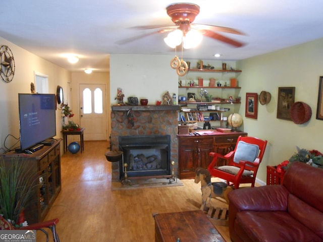 living room with ceiling fan, light hardwood / wood-style floors, and a stone fireplace