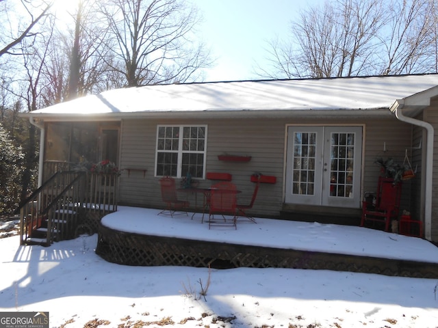 snow covered back of property with french doors and a deck