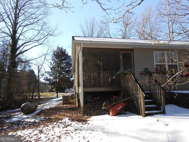 snow covered back of property with a sunroom and central AC