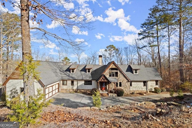 view of front of house with an attached garage, stone siding, a chimney, and concrete driveway