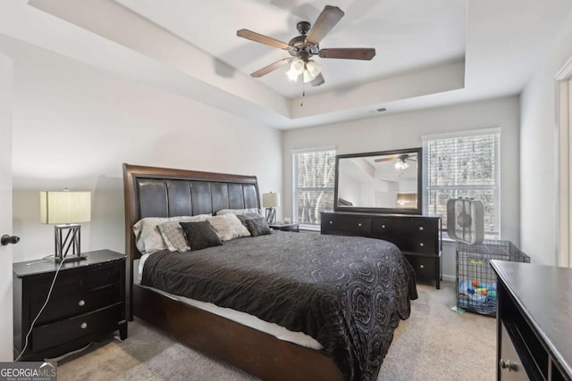 carpeted bedroom with ceiling fan, a raised ceiling, and multiple windows