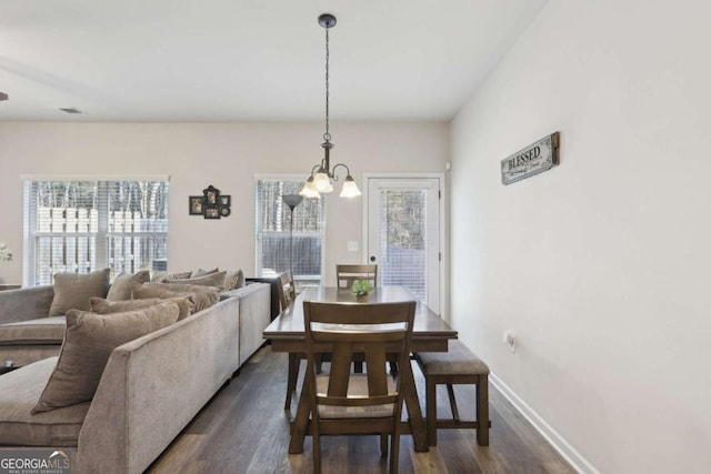 dining room with dark wood-type flooring, a wealth of natural light, and a notable chandelier