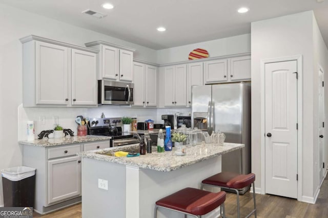 kitchen with light stone counters, sink, appliances with stainless steel finishes, and a center island with sink